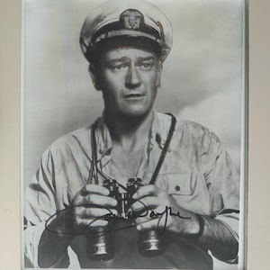 Puede incluir: Una fotografía enmarcada en blanco y negro de una persona con una gorra de estilo militar con emblema y una camisa abotonada, sosteniendo unos binoculares. La imagen presenta una firma oscura en la parte inferior de la impresión.