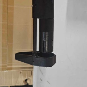 May include: Black metal gun stock with a textured grip and a black metal barrel. The stock is attached to a black metal gun.