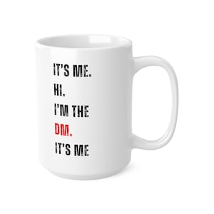 Puede incluir: Taza de cerámica blanca con texto negro que dice "It's me. Hi. I'm the DM. It's me." La palabra "DM" está en rojo.