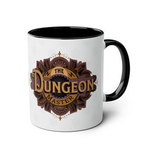 May include: White ceramic mug with a black rim and handle. The mug features a brown and purple graphic with the text "The Dungeon Master" and a stylized dice design.