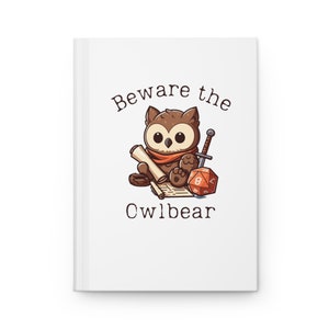May include: White journal with a cartoon owl illustration. The owl wears an orange scarf and is surrounded by a scroll, a sword, and a red and orange die. The text "Beware the Owlbear" is printed above and below the owl.