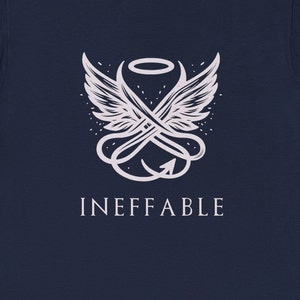 Peut inclure: Un t-shirt bleu marine avec un motif blanc. Le motif représente une paire d'ailes d'ange croisées avec une queue de diable et le mot "INEFFABLE" en dessous.