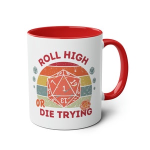 May include: White ceramic mug with a red rim and handle. The mug features a vintage-style graphic of a twenty-sided die with the text "Roll High or Die Trying".