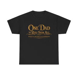 May include: Black t-shirt with gold text that reads "One Dad to Rule Them All" and "Forged in the Fires of Fatherhood". The shirt is a classic crew neck style.