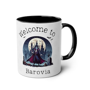 May include: White ceramic mug with a black interior and handle. The mug features a graphic of a vampire in front of a castle, with the words "Welcome to Barovia". Bats and a full moon are also depicted.