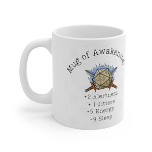 May include: White ceramic mug with a graphic of a 20-sided die with swords and flames. The text "Mug of Awakening" is written in a circle around the die. Below the die is text that reads: +2 Alertness +1 Jitters +5 Energy -9 Sleep