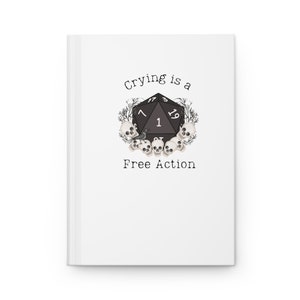 Pode incluir: Um diário branco com o texto "Crying is a Free Action" e uma ilustração em preto e branco de um dado de 20 faces rodeado de crânios.