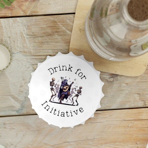 Peut inclure: Un bouchon de bouteille rond blanc avec le texte "Drink for Initiative" et une illustration en noir et blanc d'un squelette jouant du luth avec d'autres squelettes dansant autour de lui.