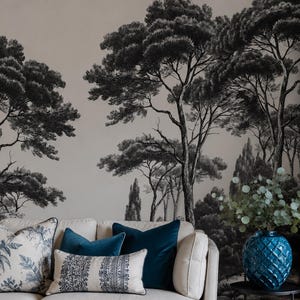 Könnte beinhalten: Ein beiges Sofa mit blauen und gemusterten Kissen, ein runder Steincouchtisch mit zwei blaugrünen, strukturierten Keramikgefäßen, einer goldenen Schale und zwei Büchern mit den Titeln Live Beautifully und This Is Home vor einer Wand mit Baumtapete.