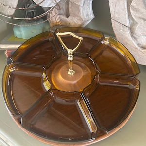 May include: A vintage serving tray with six sections, crafted from brown glass and wood. It features a gold-toned handle and a wooden base. The tray is designed for serving snacks or appetizers.
