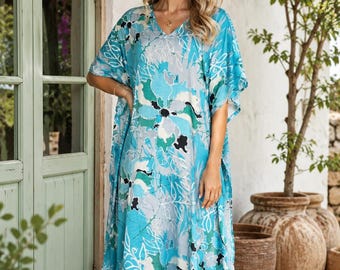May include: A floor-length kaftan dress featuring a vibrant floral pattern in shades of turquoise, teal, white, and black. The garment has a V-neckline, loose short sleeves, and a relaxed, flowing silhouette that reaches down to the lower calf area.