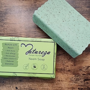 May include: A green bar of soap with the words "Natureza Pamper Yourself Neem Soap" on the packaging. The soap is on a wooden surface.