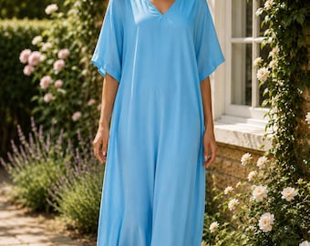 May include: A floor-length light blue kaftan dress featuring a V-neckline and loose, elbow-length sleeves. The garment is made of a lightweight, flowing fabric that drapes down to the ankles, providing a relaxed and comfortable silhouette.