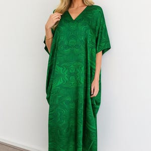 May include: A floor-length, loose-fitting kaftan dress in a vibrant emerald green hue, featuring a repeating abstract swirl pattern throughout. The garment has a V-neckline, short wide sleeves, and a relaxed, flowing silhouette that reaches the ankles.