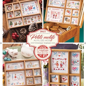 May include: A 2023 calendar agenda featuring small cross-stitch designs for each month. The calendar is titled "Petits Motifs Au Fil Des Mois" and is by Véronique Enginger. The calendar is surrounded by a wooden frame with a small wooden drawer.