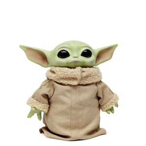 May include: A plush doll of a character with large black eyes, green skin, and large ears. The doll is wearing a tan coat with a fluffy, cream-coloured collar and cuffs. The doll is standing against a white background.