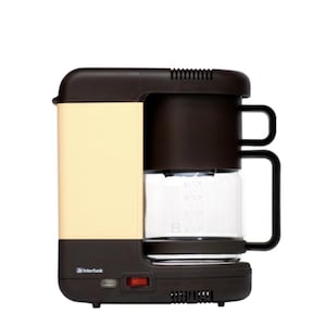 May include: A retro-style coffee maker in cream, brown, and black. The appliance features a glass carafe with measurement markings, a red power button, and the "Interfunk" logo. The coffee maker has a rectangular design with a handle on each side.