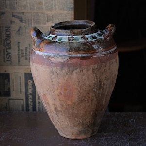 May include: A large, brown, earthenware pot with a wide mouth and two handles. The pot has a decorative band of green and white painted leaves around the top.