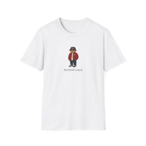 May include: White t-shirt with a cartoon bear wearing a red jacket, black trousers, and a bucket hat. The text "Sheffield United" is printed below the bear illustration. The shirt is made of a soft, comfortable material.