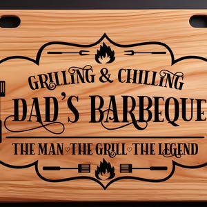 May include: A wooden cutting board with an engraved design that says "Grilling & Chilling Dad's Barbeque The Man The Grill The Legend".