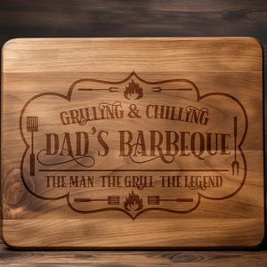 May include: A wooden cutting board with an engraved design that says "Grilling & Chilling Dad's Barbeque The Man The Grill The Legend".