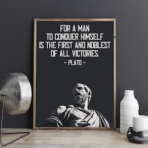 May include: A black and white framed print with a quote by Plato: "For a man to conquer himself is the first and noblest of all victories." The quote is centered on a black background with a white silhouette of Plato's head at the bottom.