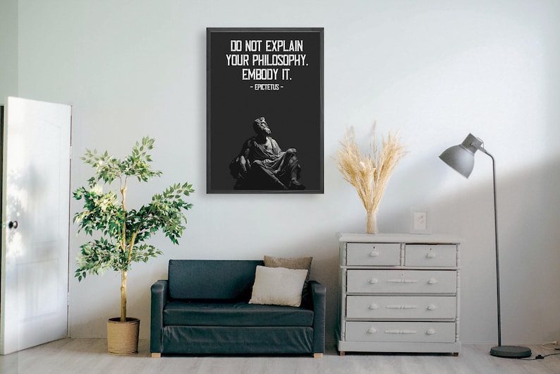 Puede incluir: Impresi&oacute;n enmarcada en blanco y negro con una cita de Epicteto: "No expliques tu filosof&iacute;a. Enc&aacute;rnala." La cita est&aacute; centrada en un fondo negro con una estatua blanca de un hombre sentado en una silla en el fondo.