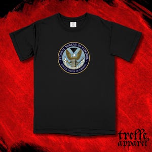 May include: Black t-shirt featuring a circular emblem with the text "FEDERAL BUREAU OF CONTROL" and "UNITED STATES OF AMERICA." The emblem includes an eagle, a triangle, and other design elements. The shirt has short sleeves and a crew neck.