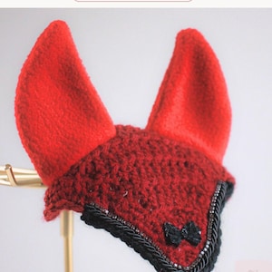 May include: A red crochet horse ear bonnet featuring two upright red ears, a dark red crocheted front panel, a black braided trim, and a small black bow accent. The text Crimson Charm is visible at the top, and the Aurora Rose logo is at the bottom.
