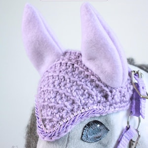 May include: A lavender crochet horse ear bonnet featuring two upright felt ears, a textured knit pattern, and a decorative trim of small beads and twisted cord. The text Lavender Mist, Aurora Rose, and Autumn/Winter 2026 Moonlit Manor Collection appear.