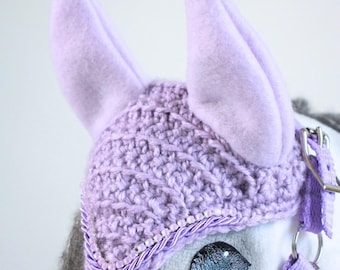 May include: A lavender crochet horse ear bonnet featuring two upright felt ears, a textured knit pattern, and a decorative trim of small beads and twisted cord. The text Lavender Mist, Aurora Rose, and Autumn/Winter 2026 Moonlit Manor Collection appear.
