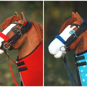 May include: A model horse head featuring a brown coat, white blaze, and yarn mane. It wears a black bridle with a red noseband and a red blanket, or a black bridle with a blue noseband and a light blue blanket with white polka dots.