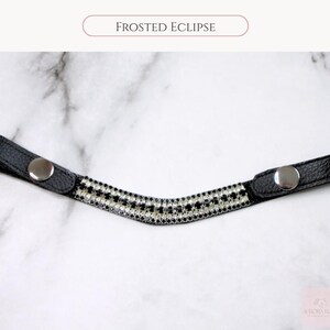 May include: A black leather browband with a curved, decorative center. The center is adorned with a pattern of alternating black and clear rhinestones. The browband has silver snap closures and the text "FROSTED ECLIPSE".