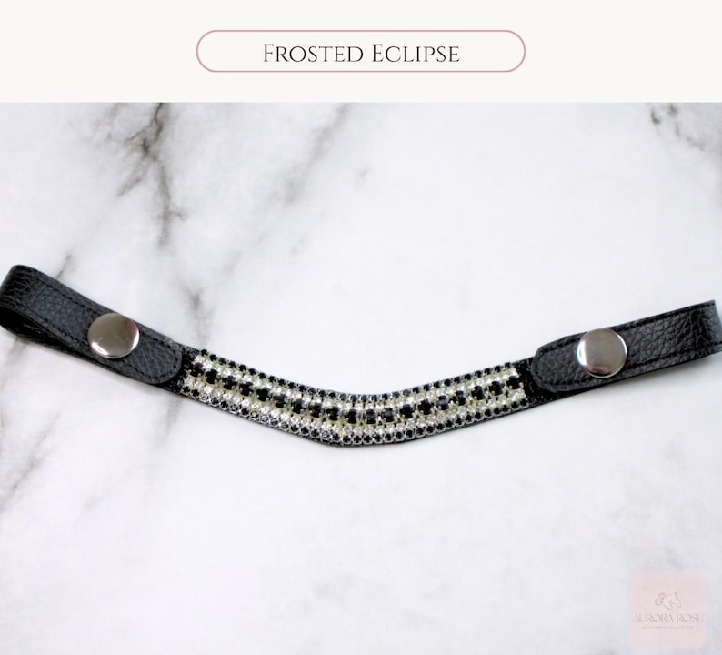 May include: A black leather browband with a curved, decorative center. The center is adorned with a pattern of alternating black and clear rhinestones. The browband has silver snap closures and the text "FROSTED ECLIPSE".