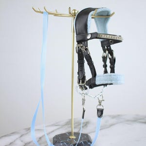 May include: A black leather horse bridle featuring light blue fleece padding on the crown and noseband, a browband adorned with clear crystals, silver-toned metal buckles, and a long, light blue nylon lead rope attached with silver metal clips.