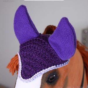 May include: A purple crochet horse ear bonnet with fleece ears and a light purple trim. The item is labeled AMETHYST VEIL and features a textured knit pattern. It is designed to fit over the ears and forehead of a horse, providing a secure fit.
