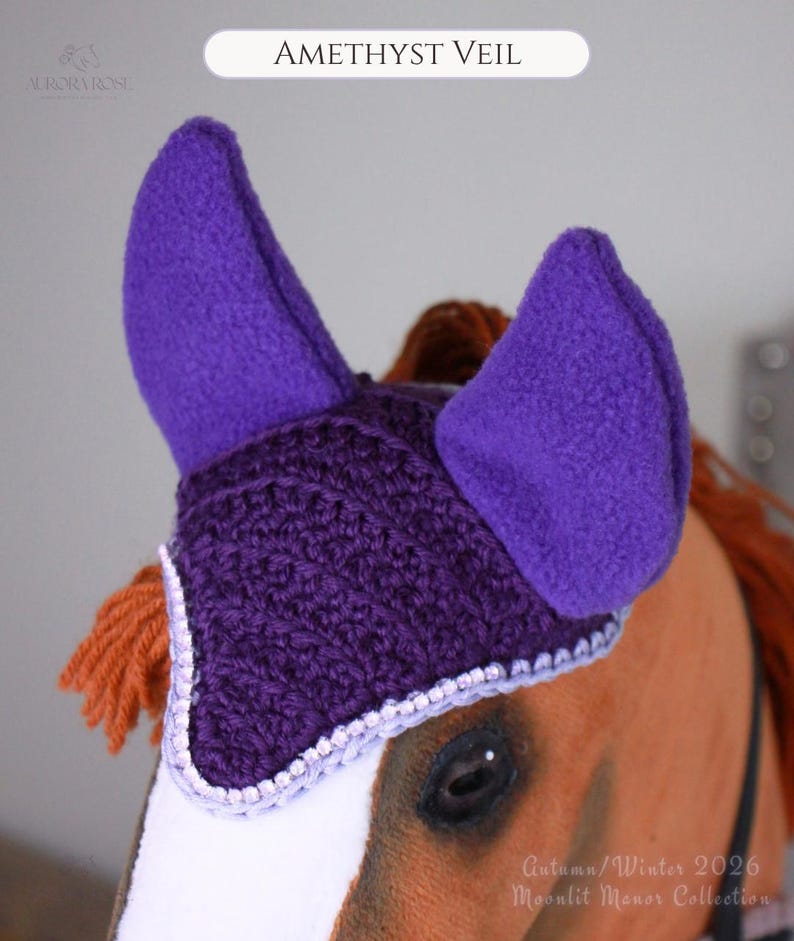 May include: A purple crochet horse ear bonnet with fleece ears and a light purple trim. The item is labeled AMETHYST VEIL and features a textured knit pattern. It is designed to fit over the ears and forehead of a horse, providing a secure fit.