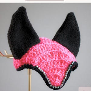 May include: A crochet horse ear bonnet featuring a bright pink textured center and two tall, solid black ears. The front edge is lined with a row of iridescent, multi-colored crystals. The text "PUNK PRINCESS" appears at the top of the image.