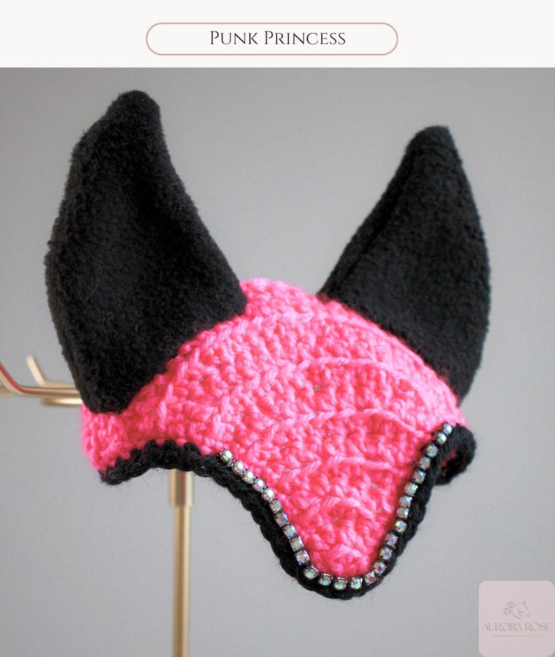 May include: A crochet horse ear bonnet featuring a bright pink textured center and two tall, solid black ears. The front edge is lined with a row of iridescent, multi-colored crystals. The text "PUNK PRINCESS" appears at the top of the image.