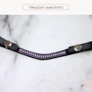 May include: Black leather browband with a row of purple rhinestones. The browband has silver snap closures on each end. The text "TWILIGHT AMETHYST" is printed at the top of the image.