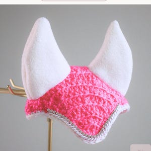 May include: A bright pink crocheted horse ear bonnet featuring two tall white fleece ears. The front edge is decorated with a silver braided trim embedded with small clear rhinestones. The text Sugar Spark appears at the top of the image.