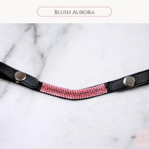 May include: Black leather browband with pink rhinestones and silver snap closures. The text "BLUSH AURORA" is displayed above the browband. This browband is designed for equestrian use.