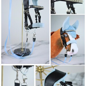 May include: A black leather horse bridle featuring light blue fleece padding, silver-toned metal hardware, and a browband encrusted with clear crystals. The set includes a light blue lead rope and a matching light blue ear bonnet for a horse.