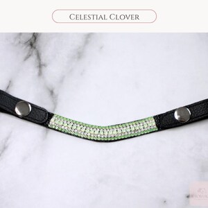 May include: Black leather browband with a curved design, adorned with rows of sparkling light green and clear crystals. The browband has silver snap closures on each end. The text "CELESTIAL CLOVER" is displayed above the browband.
