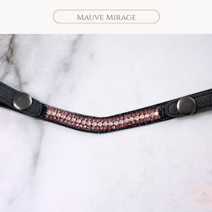 May include: A black leather browband with a row of pink and clear crystals. The browband has silver snap closures on each end. The text "MAUVE MIRAGE" is above the browband.