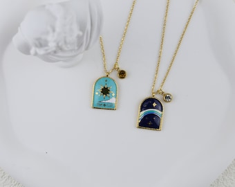 May include: Two gold necklaces with enamel pendants. One pendant is blue with a rainbow and stars, the other is turquoise with a sun and clouds. Both pendants have gold accents and the text "The Sun" and "The Moon".