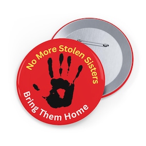 Puede incluir: Botón rojo con una huella de mano negra y el texto "No More Stolen Sisters Bring Them Home" en amarillo.