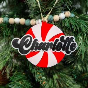May include: A red and white candy cane ornament with the name "Charlotte" written in black cursive lettering.