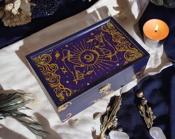 May include: A wooden box with a dark blue lid and gold accents. The lid features a celestial design with a sun, moon, and stars. The box is ideal for storing small items such as jewellery or trinkets.