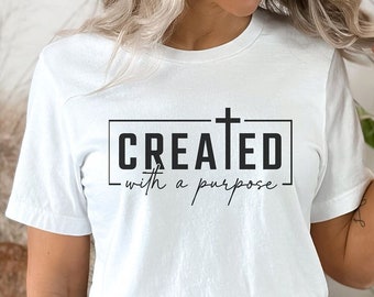 Puede incluir: Camiseta blanca con un gráfico negro que dice "CREATED with a purpose" y una cruz sobre la palabra "CREATED".